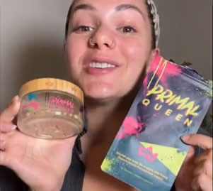 Person holding Primal Queen skincare products, smiling at the camera.